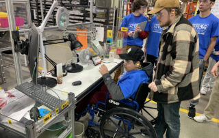 Multiple students, including one in a wheelchair, surround a workbench