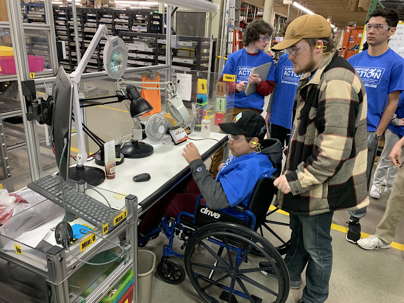 Multiple students, including one in a wheelchair, surround a workbench