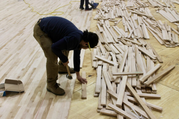A man works with planks of wood on the ground