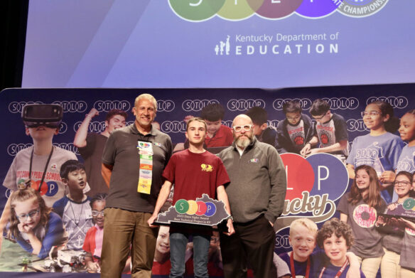 Picture of a student on stage holding an STLP trophy, standing beside two Kentucky Department of Education staff members.