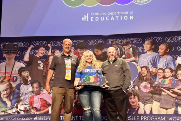 Picture of a student on stage holding an STLP trophy, standing beside two Kentucky Department of Education staff members.