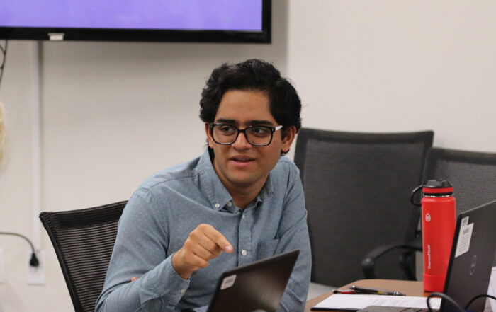 A man points down at a table as he speaks