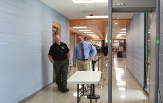 Two men stand by a door and smile as a metal detector stands in front of them