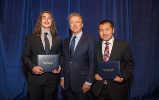 Three men stand for a photo while two of them men hold certificates