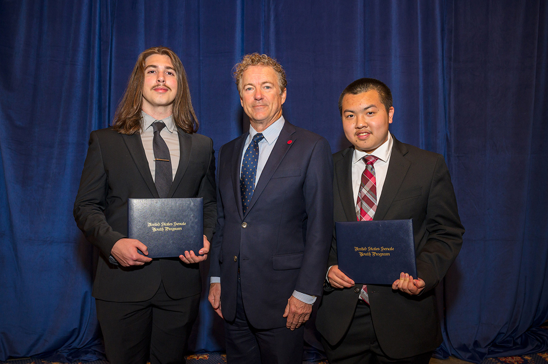Three men stand for a photo while two of them men hold certificates