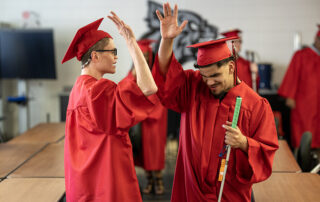 Picture of Alex Hitzelberger and Cory Wallace giving each other a high five in their graduation caps and gowns.
