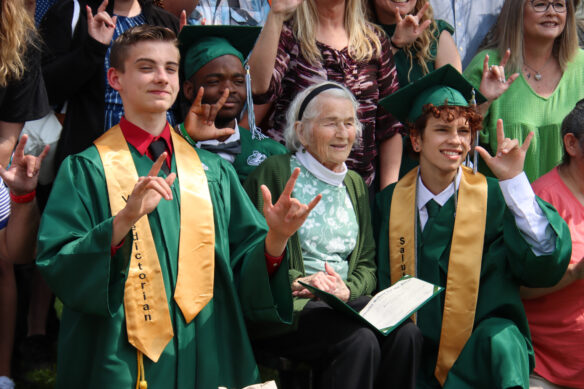 Multiple people pose for a photo while holding up the American Sign Language sign for I Love You