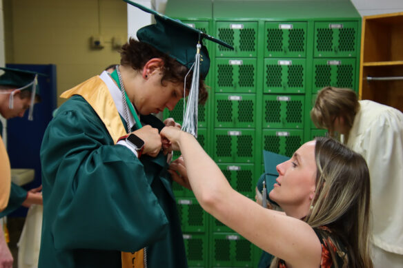 A woman adjusts another person's graduation gown