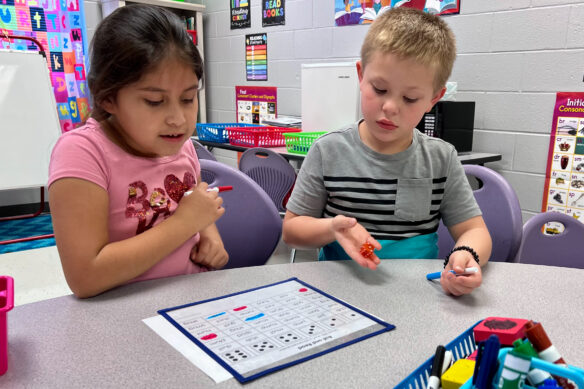 Two elementary students use dice to help them pick a word on a worksheet.