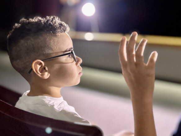 A boy sits in an auditorium, He has his hand rasied.