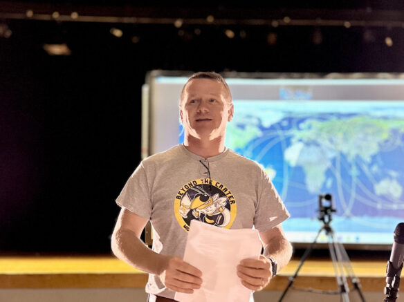 A man is standing, talking to an audience. He is holding a piece of paper.