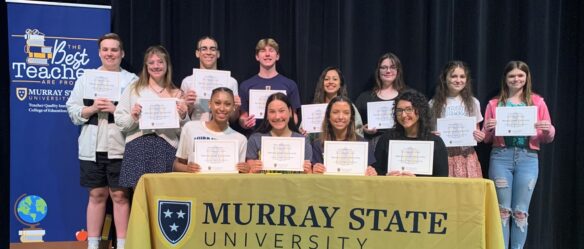 A group of students hold pieces of paper to show they have committed to Murray State University for teaching