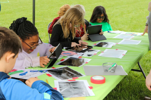 Photo of students working on iPads at a table outdoors