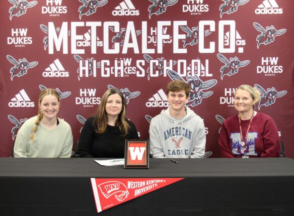 A student smiles at a table that has a Western Kentucky University banner in the background.