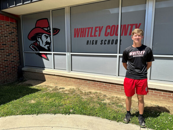 Picture of a young man standing in front of a school, with the words Whitley County High School on the windows behind him.