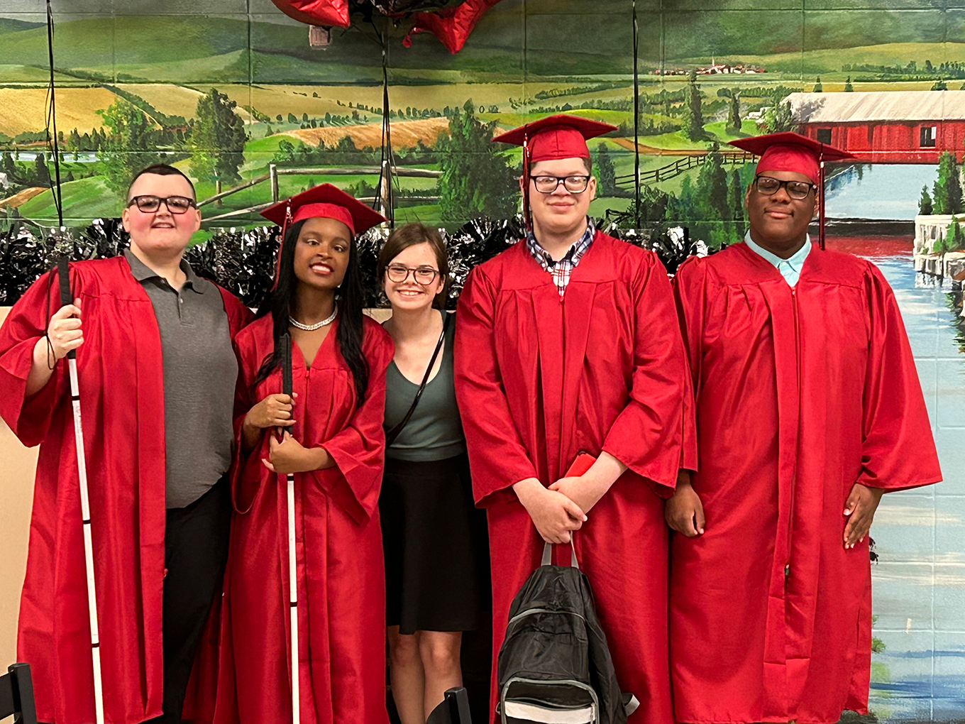 Five people, including four in red graduation gowns, pose for a photo
