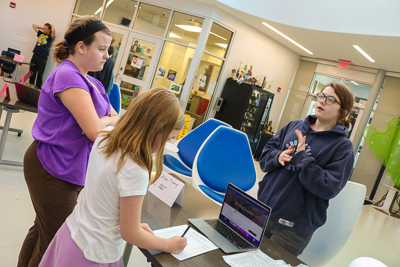 A group of kids stand around a table with computers and notepads on it