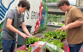 Picture of two students working outside at a metal picnic table, putting lettuce into plastic bags.