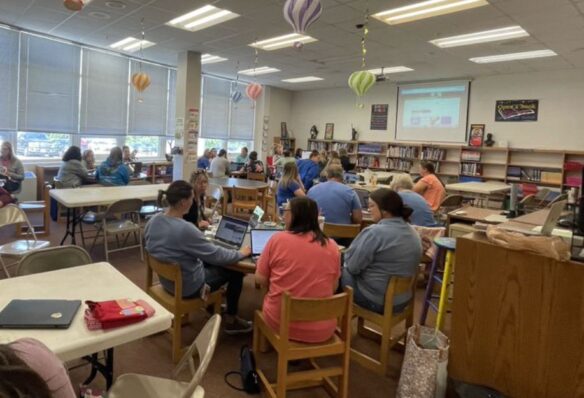 A group of teachers sitting at tables in a library are working together.