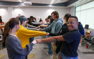 Two lines of students face each other, giving fist bumps. A young male student nearest the camera smiles for the picture.