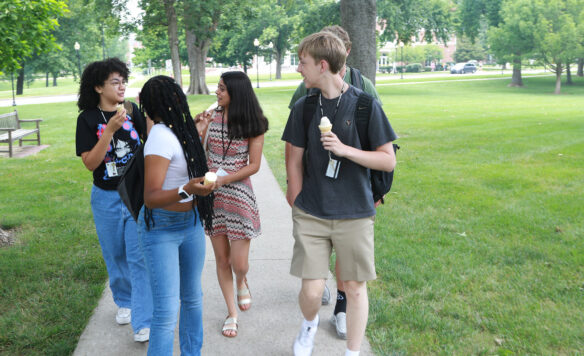 High school, students Janelle Pitmon, Kadi’ah Malone, Anya Sharma, Brayden Warren and Gillam Nicodemus walk along a sidewalk holding ice cream cones and talking to each other.