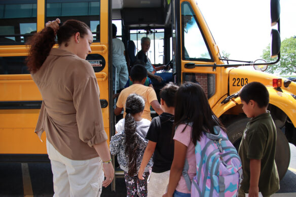 A woman stands as a group of kids walks onto a bus.