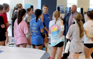 Willis Foster talking to a group of female volley ball players in a school cafeteria.