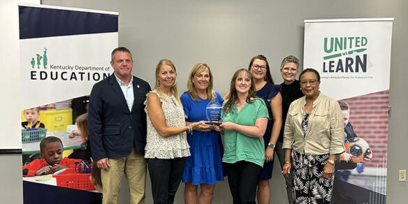 Jason Glass and Sharon Porter Robinson stand with a group of five smiling women who are holding onto a glass trophy.