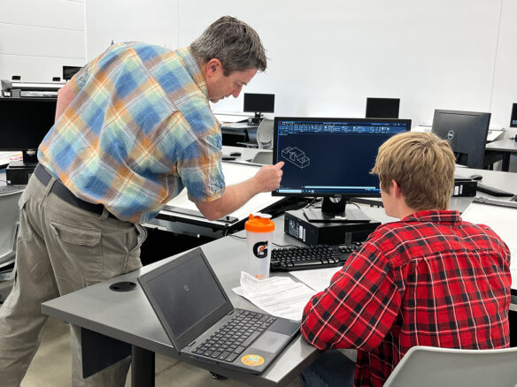 A teacher points at a computer screen as a student looks on