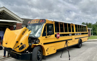 Picture of a bus with its hood up, sitting in front of a school building.
