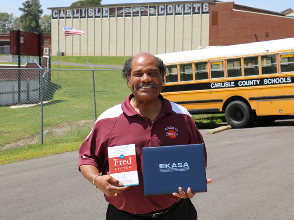 Carlisle County school bus driver Mahlon Thomas smiles with an award and a book in his hands