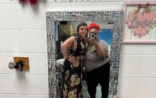 A teacher and female student take a picture together in a classroom mirror.