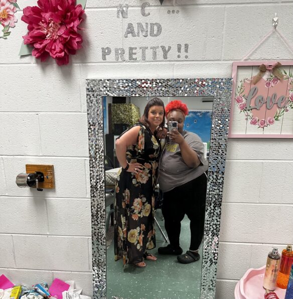 A teacher and female student take a picture together in a classroom mirror.