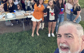 A group of smiling students at a buffet table stand behind Superintendent Todd Neace as he takes a selfie.