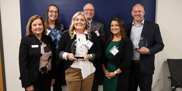 Robin Kinney smiles along with the award winners, who are holding glass trophies.