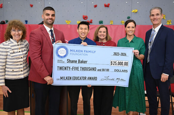 A small group of smiling people stand in a gym holding a large, ceremonial check.