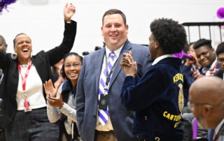 Carter G. Woodson Academy teacher Jacob Ball reacts in shock as learns he just won $25,000 from the Milken Family Foundation. He is surrounded by his students.