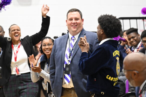 Carter G. Woodson Academy teacher Jacob Ball reacts in shock as learns he just won $25,000 from the Milken Family Foundation. He is surrounded by his students.