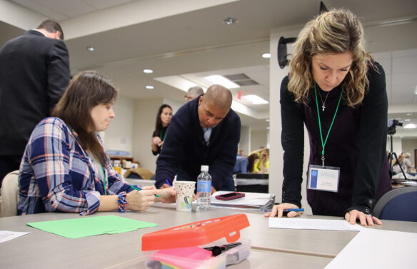 Three people surround a table while each is writing something on pieces of paper