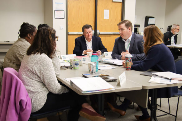 Five people discuss something while sitting at a table