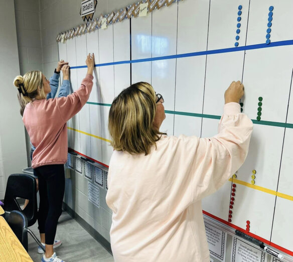 Two people place colored dots on a white board