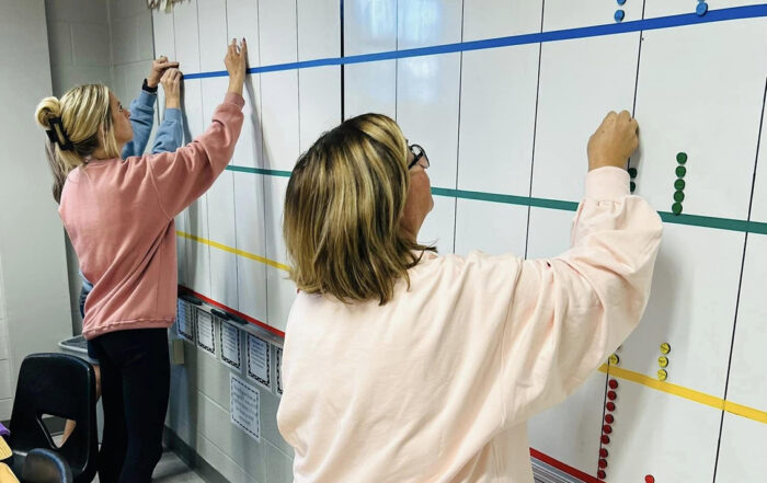 Two people place colored dots on a white board