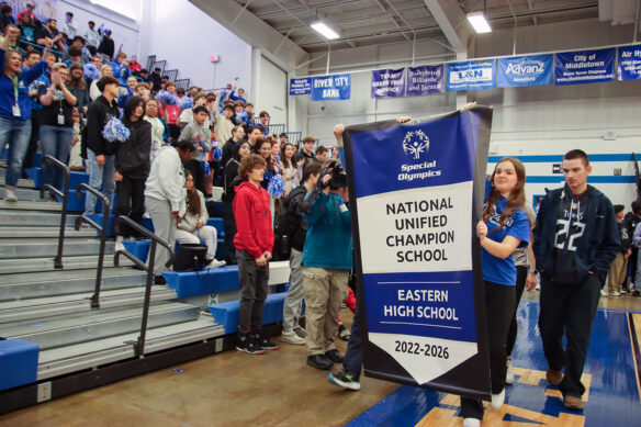 Students hold a banner saying National Unified Champion School - Eastern High School in front of a crowd of students