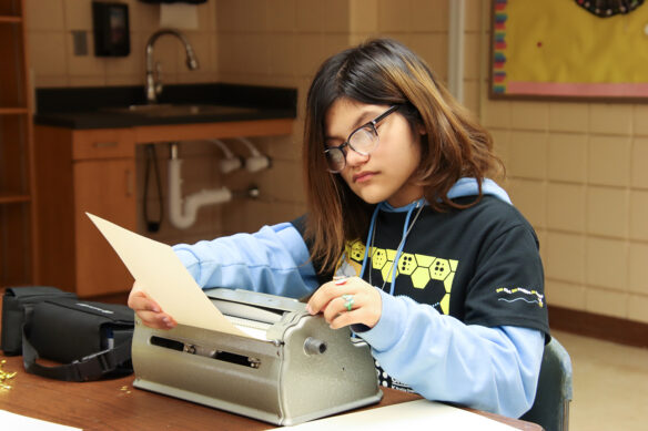 A student feeds paper into a braille machine
