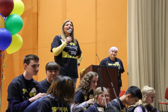 A woman speaks into a microphone with kids sitting in front of her