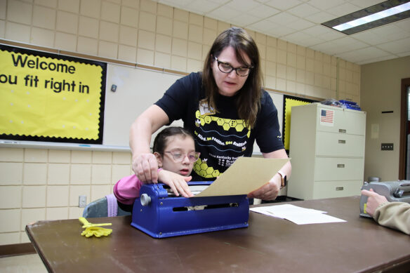 A woman helps a kid feed paper into a braille machine
