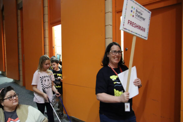 A woman holding a sign that says "freshman" lead students into an auditorium