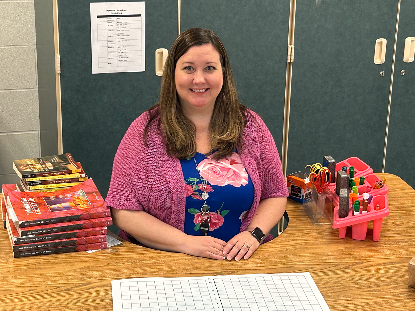 A woman sits at a desk with books near her