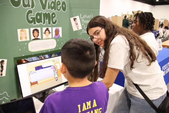 A student shows another student her project, a coding game, at the STLP State Championships