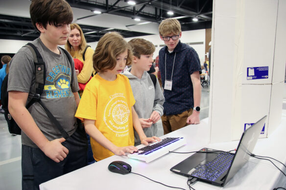 Four students and a woman hover around a laptop